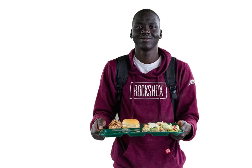 A young man in a maroon hoodie carries a cafeteria tray with a meal.
