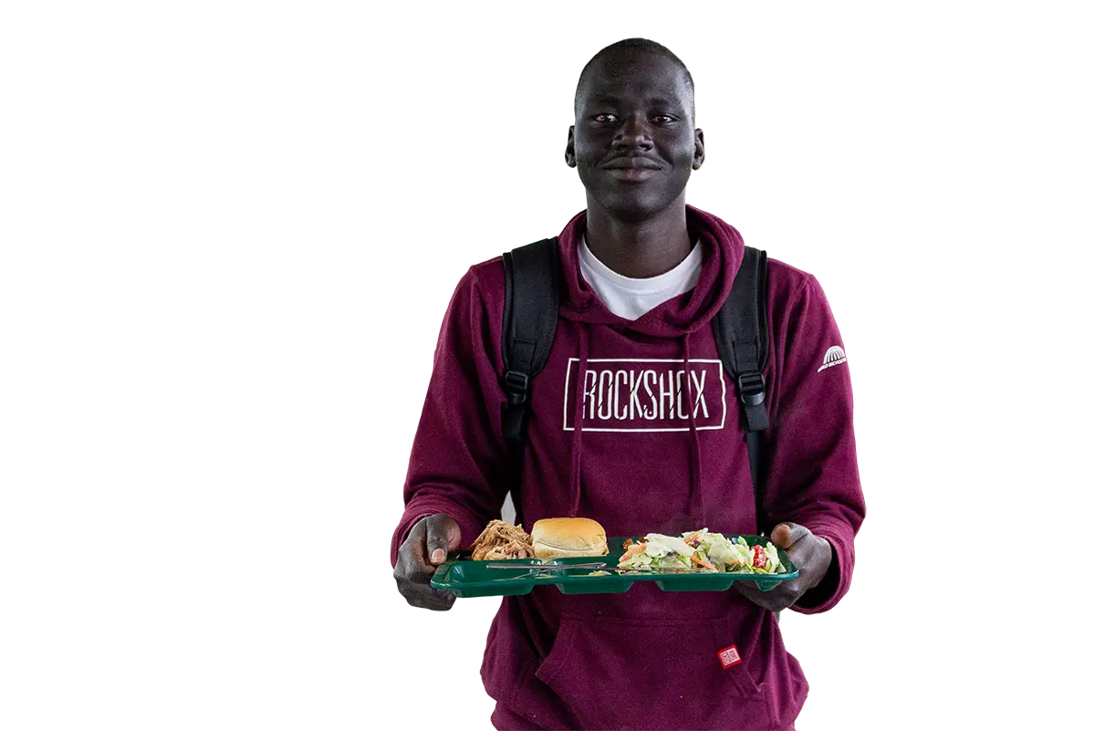 A young man in a maroon hoodie carries a cafeteria tray with a meal.